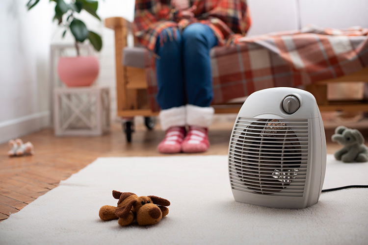 Someone sitting on a couch in front of a space heater.